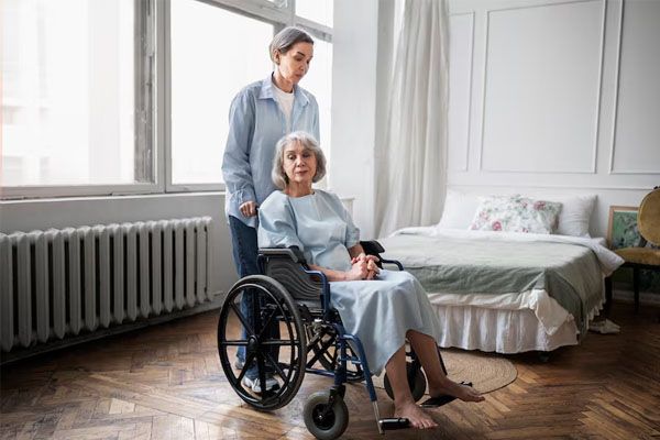 Donna anziana in sedia a rotelle spinta da una donna nella stanza