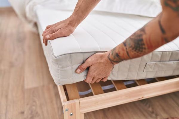 braccia tatuate di un giovane che mette un materasso su un letto