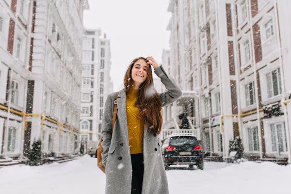Donna con un cappotto moderno in piedi su una strada innevata