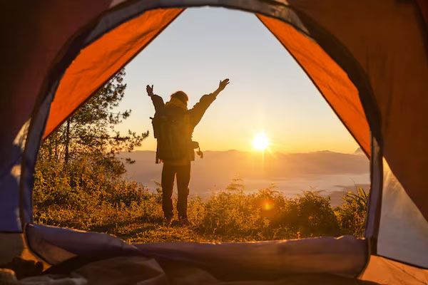 Escursionista di montagna con zaino e braccia tese davanti alla tenda arancione