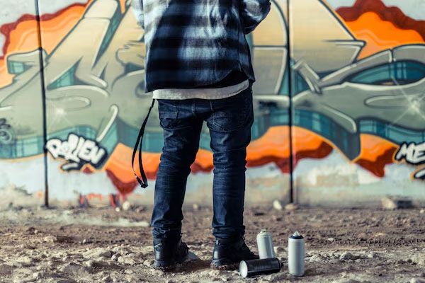 artista della sezione inferiore in piedi vicino a una bomboletta spray davanti a un muro di graffiti