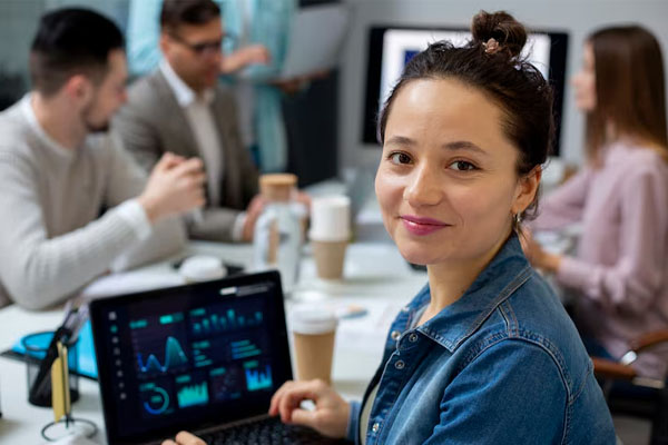Un giovane guarda una riunione di lavoro con il monitor di un computer portatile, con un gruppo di persone 